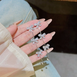 Detailed view of silver bow tassel earrings with sparkling zircon held by hand model