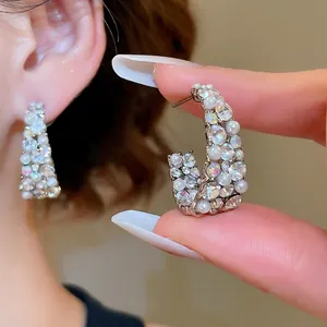 Sparkling silver needle C-shaped earrings with pearls and rhinestones shown on ear and hand