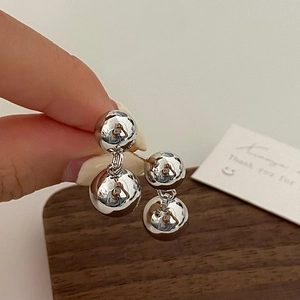 Close-up of minimalist silver double-sphere drop earrings with a polished mirror finish