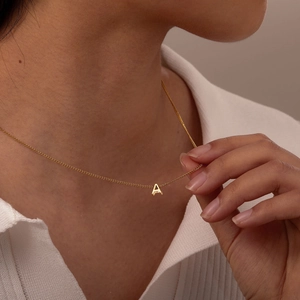 Close-up of a gold capital A letter pendant on a refined chain worn by a model