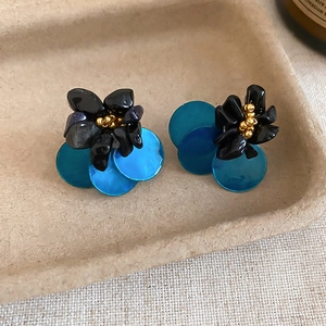 Detailed view of floral shell stud earrings with blue sequins and black beads center