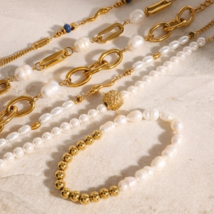 Luxurious gold-plated stainless steel necklace and pearl bracelet set on a stone surface