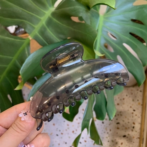 Detail of translucent smoky grey hair claw clip held over a lush green monstera leaf
