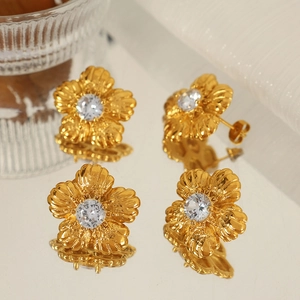 Vintage gold flower stud earrings with a central clear zircon on a reflective surface