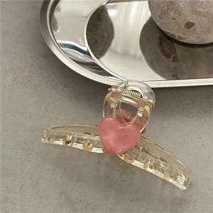 Macro shot of a pink heart hair claw clip with golden spring on a textured grey surface