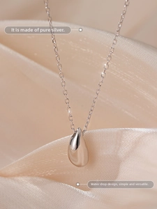 Macro shot of s925 sterling silver water drop pendant necklace on champagne silk fabric
