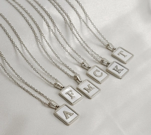 Macro detail of silver square shell necklaces with A, F, M, C, K, T letter pendants on silk