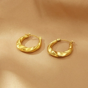 Detail of gold twisted texture hoop earrings on beige silk fabric background