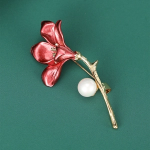 Close-up of red enamel trumpet flower brooch with gold stem and pearl on green texture