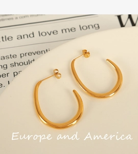 Detail of chunky gold U-shaped hoop earrings on white ceramic plate with retro newspaper