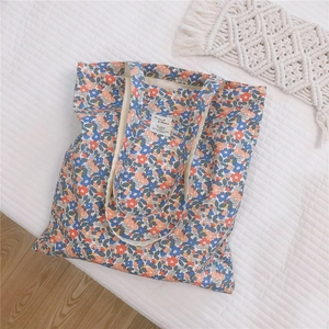 Flat lay of a floral cotton tote bag with blue and orange prints on quilted bedding