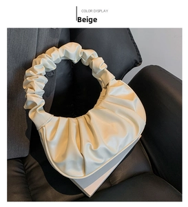 Detail of beige pleated handbag with organza-style folds on a sleek black leather sofa