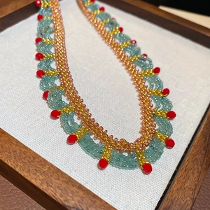 Close-up of handmade beaded lace necklace with turquoise and red crystal details