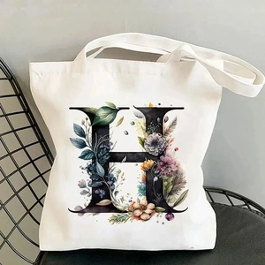 Detailed close-up of white canvas tote bag with floral letter H on a black chair