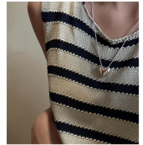 Detailed view of a silver heart pendant necklace on a model with a striped sweater