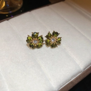 Macro view of vintage dark green flower earrings with diamonds on white velvet padding