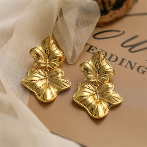 Detailed view of large golden maple leaf earrings on silk fabric and brown background