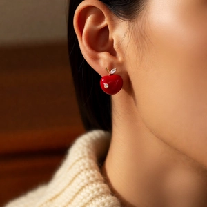 Close-up of a red cherry apple stud earring with zircon leaf worn by a model