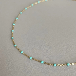 Close-up of a delicate gold chain necklace featuring small sky blue beaded accents