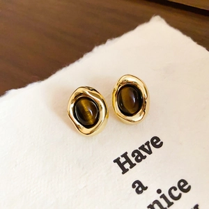 Macro shot of gold-plated earrings with deep brown tiger eye stone on textured paper
