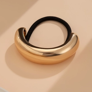 Detail of a U-shaped golden metal clip with a black elastic hair band on beige background
