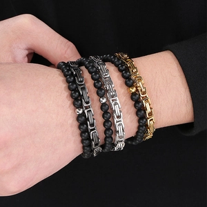 Close-up of stacked black matte beads and multi-tone Byzantine chain bracelets on wrist