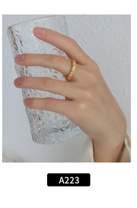 Close-up of golden irregular textured ring worn by a model holding a glass cup
