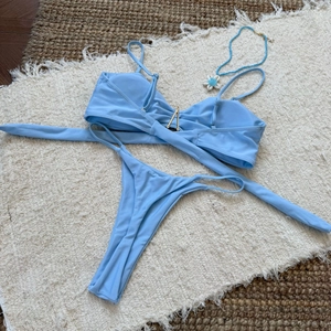 Light blue bikini top with gold V-hardware detail on textured woven beach mat
