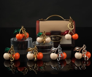 Detailed view of cherry bag charms with resin beads and metallic leaves on a black surface