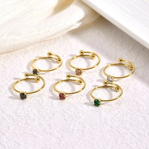 Set of six gold plated open rings featuring multi-colored gemstones on white rock surface