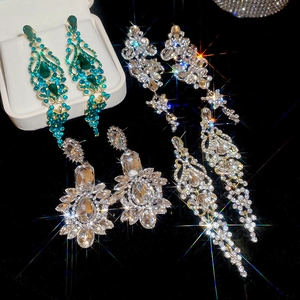 Close-up of luxury green gemstone and rhinestone drop earrings with sparkling starburst effect