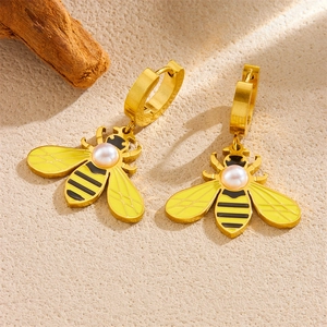 Golden bee hoop earrings with yellow enamel, white faux pearls on textured background