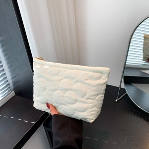 Quilted floral cotton cosmetic bag in cream with gold zipper held by hand near a mirror