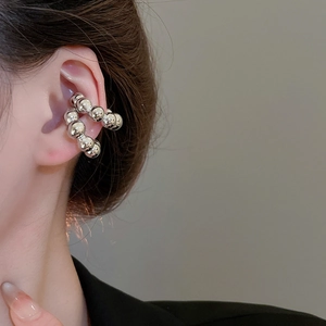 Dettaglio macro di un ear cuff argento a forma di C con sfere lucide sull'orecchio