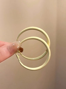 Detail view of large pale yellow enamel hoop earrings held against a neutral background