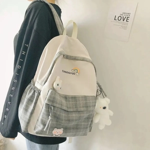 Side view of checkered canvas backpack with a plush bear charm on a female model