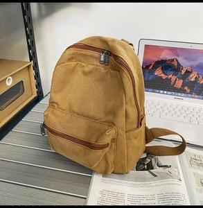 Detailansicht eines senfgelben Canvas-Rucksacks auf Metalltisch mit Laptop-Hintergrund