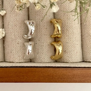 Detailed view of gold and silver wavy C-shaped earrings on a textured linen background