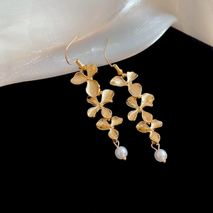 Detail showing cascading gold flower petals with a white pearl on minimalist silk background