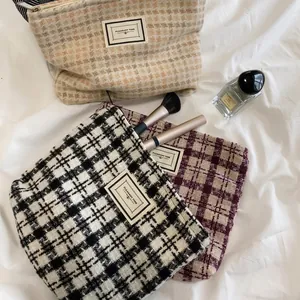 Large plaid tweed cosmetic bags in black, beige, and red on white sheets