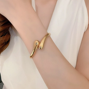 Close-up of a minimalist golden waterdrop cuff bracelet on wrist with glossy finish
