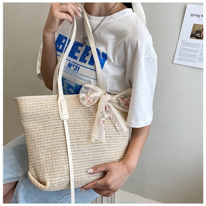 Close-up of beige straw tote bag featuring white lace bow and pink floral embroidery