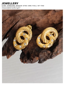 Detailed view of intertwined gold hoop earrings with small white rhinestones on rustic wood