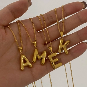 Detail of gold letter pendants A M E K on beaded necklaces worn on the neck