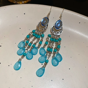 Detailed macro view of bohemian lake blue tassel earrings with silver beads on a white tray