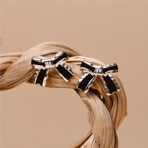 Elegant 925 sterling silver bow earrings with black enamel on a natural texture