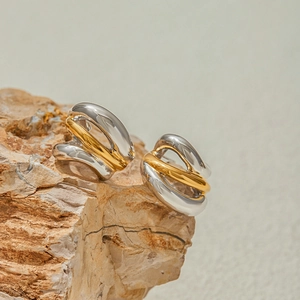 Detailed close-up of mixed gold and silver two-tone C-shape earrings on stone display
