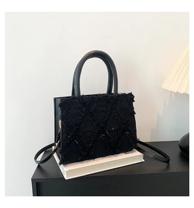 Detail of black quilted tote bag with fringe edges, round leather handles and shoulder strap