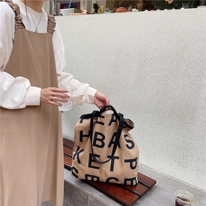 Detail of camel canvas tote bag with black logo on a wooden bench outdoors