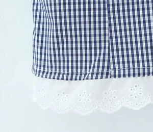 Detailed close-up of blue and white gingham fabric with white eyelet embroidery trim